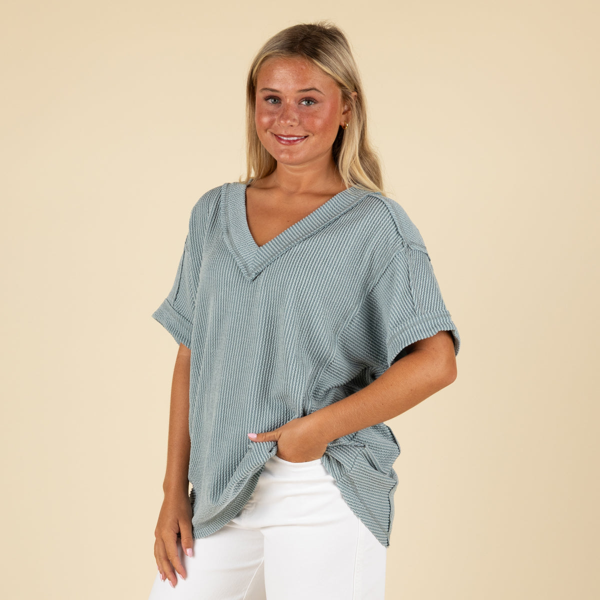 front view of a woman wearing an oversized slate blue ribbed vneck top paired with white denim jeans.