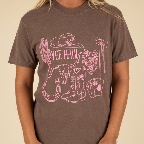 Person wearing a brown t-shirt with pink Western-themed graphics and text.