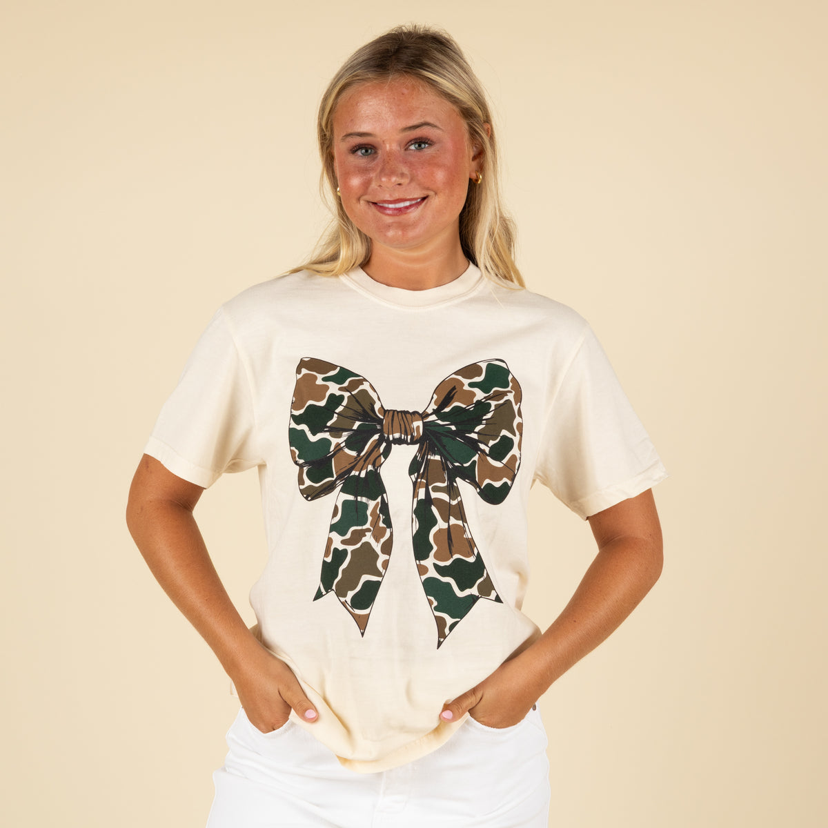 Woman wearing a beige t-shirt with a camouflage bow design on a beige background