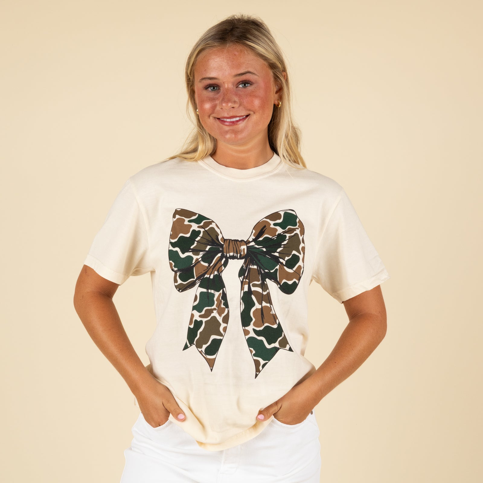 Woman wearing a beige t-shirt with a camouflage bow design on a beige background