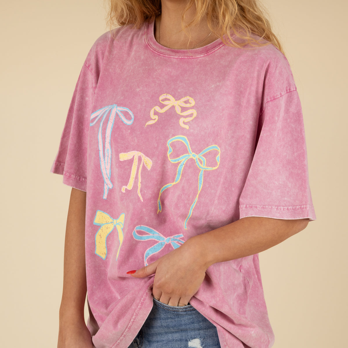 Person wearing a pink t-shirt with colorful bow designs on a beige background