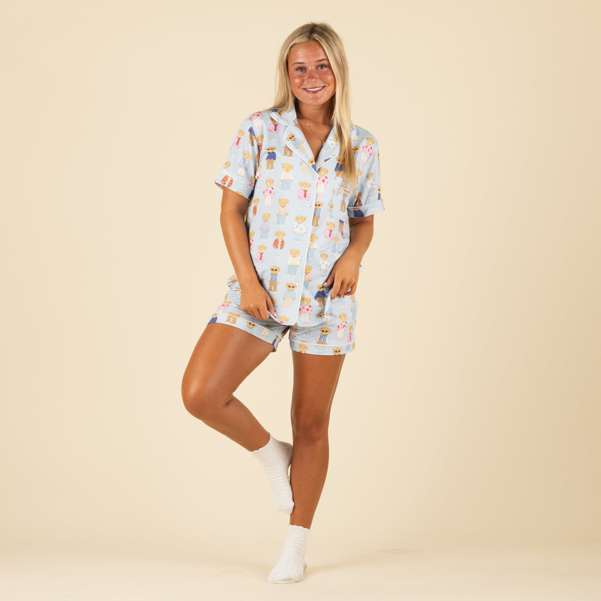 Woman standing in full view wearing matching teddy bear pajama set and white socks, smiling at camera