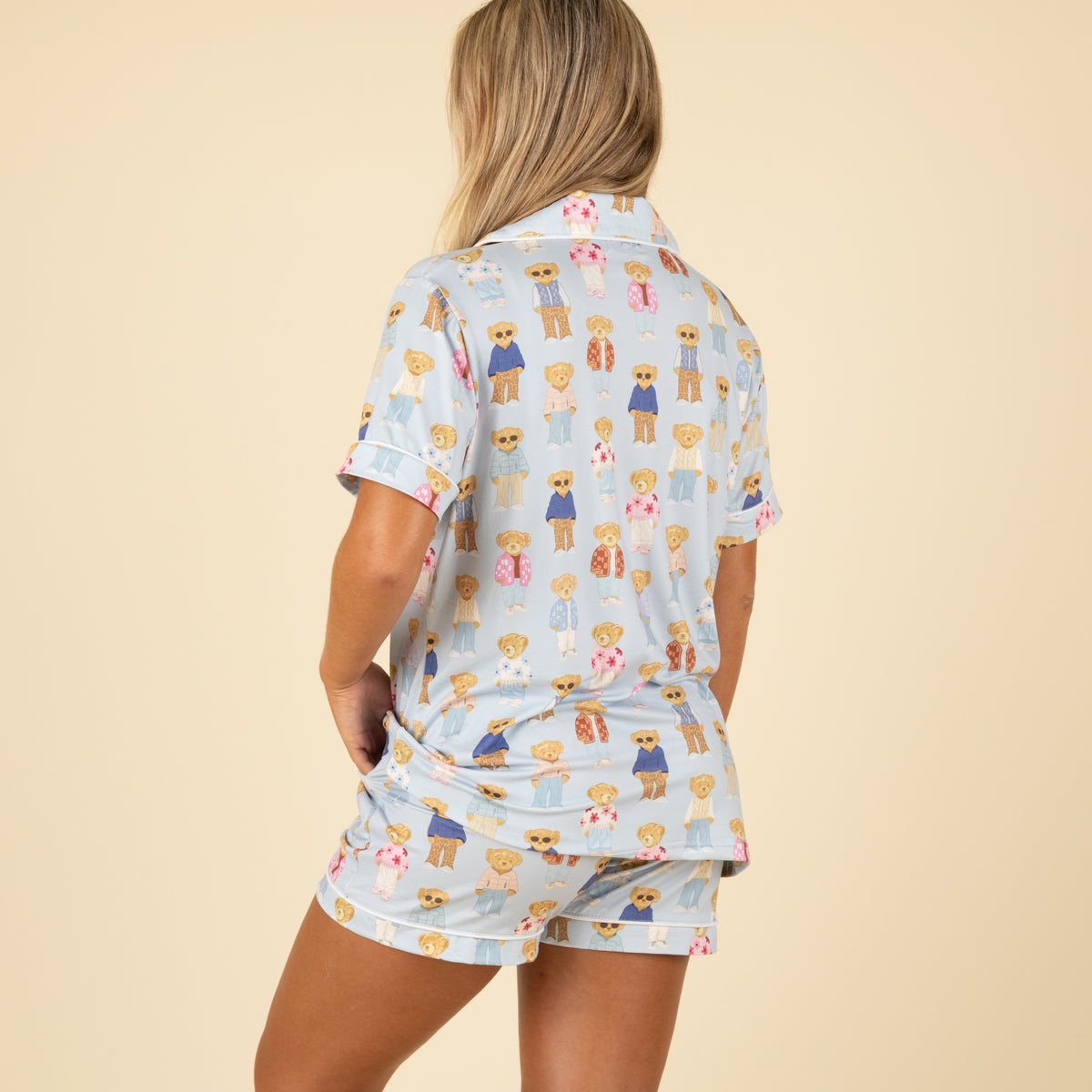 Three-quarter back view of woman wearing full teddy bear print pajama set with hands in pockets