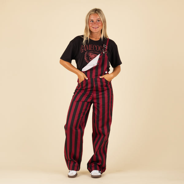 Front view of woman wearing garnet and black striped overalls with front pocket and silver hardware over a black Gamecocks tee.