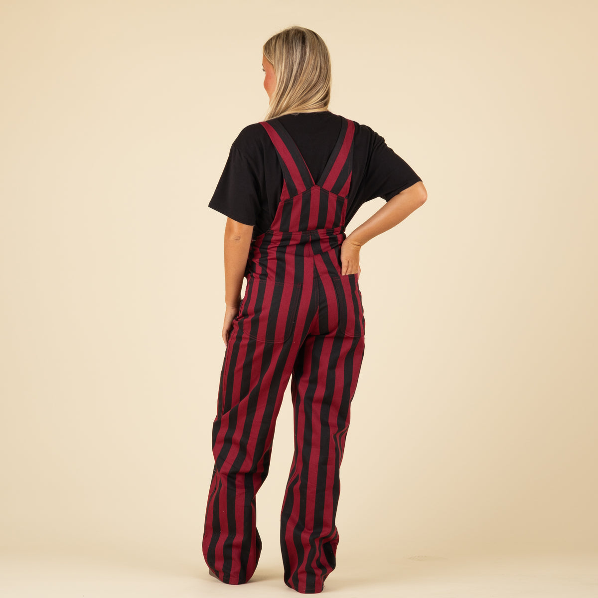 Back view of woman wearing garnet and black vertically striped overalls with crisscross straps over a black Gamecocks t-shirt.