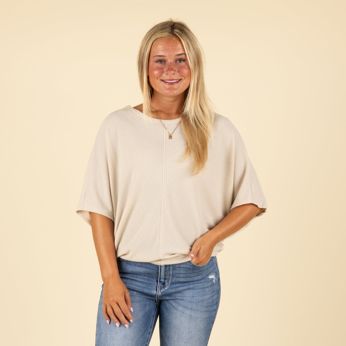 Front view of model wearing light beige ribbed short sleeve cocoon top with center seam and relaxed fit.