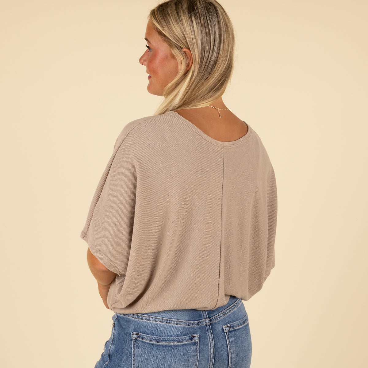Woman wearing a beige top and blue jeans on a beige background