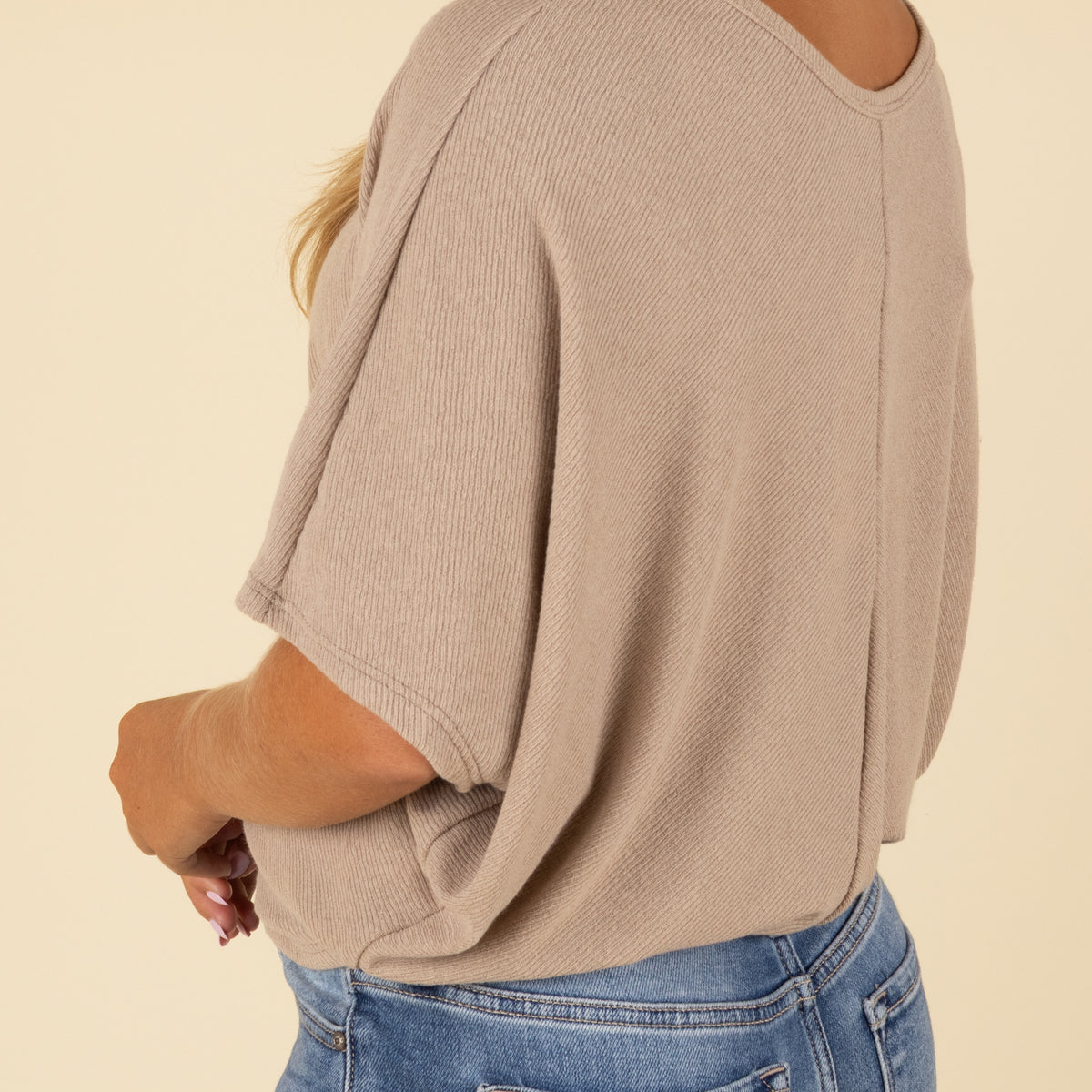 Person wearing a beige ribbed sweater and blue jeans on a beige background