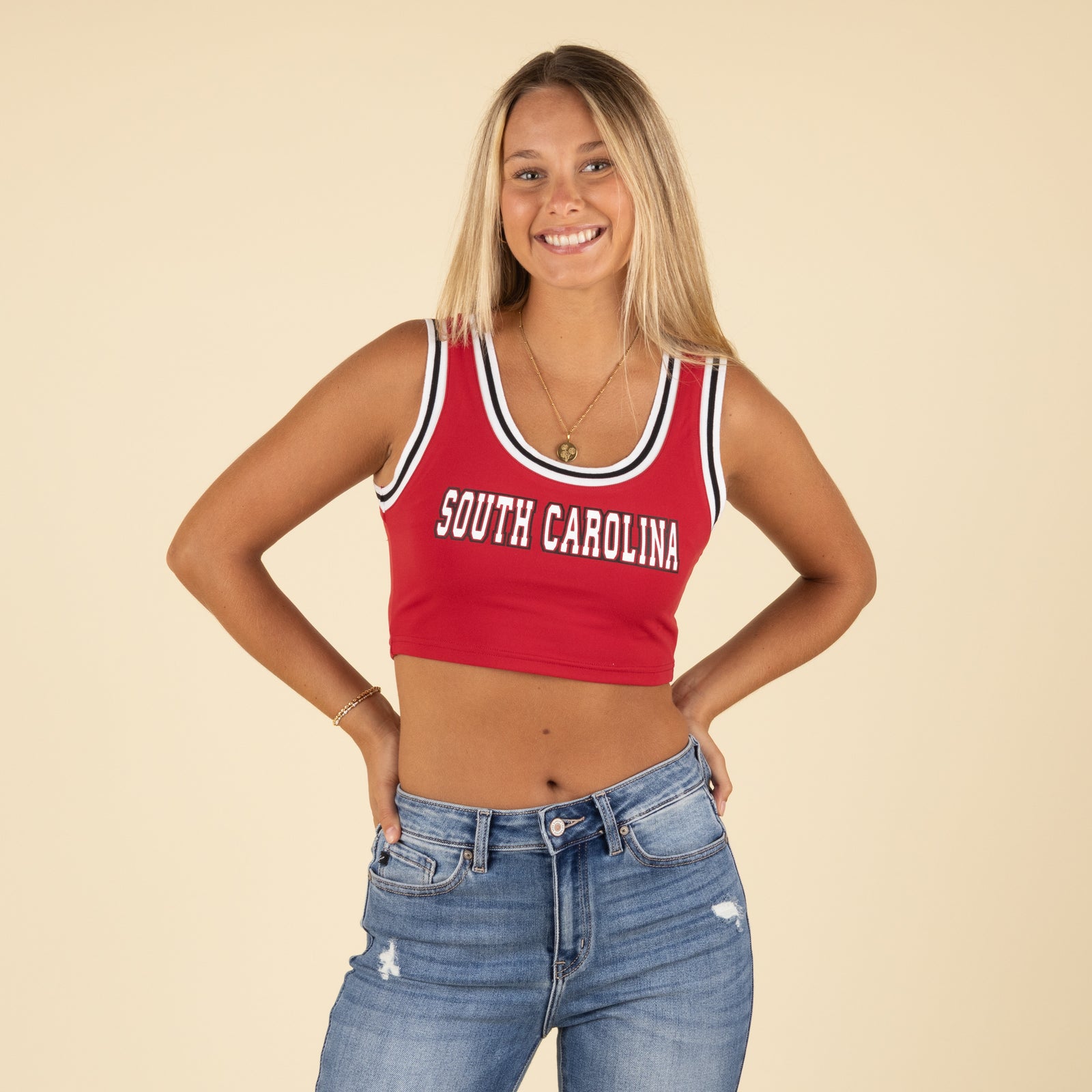 Front view of a woman smiling and wearing a red South Carolina crop tank top with striped trim and distressed blue jeans.