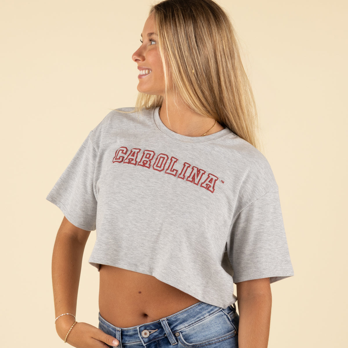 Side view of a woman wearing a grey Carolina cropped t-shirt with red collegiate lettering and light-wash jeans.