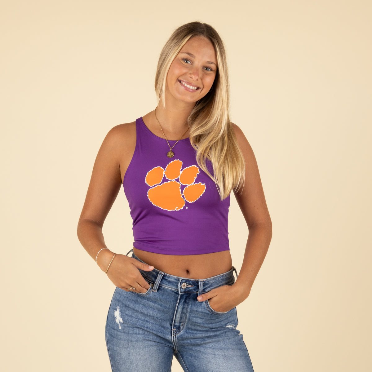 Woman smiling in a purple Clemson crop tank with orange paw print and hands in pockets.