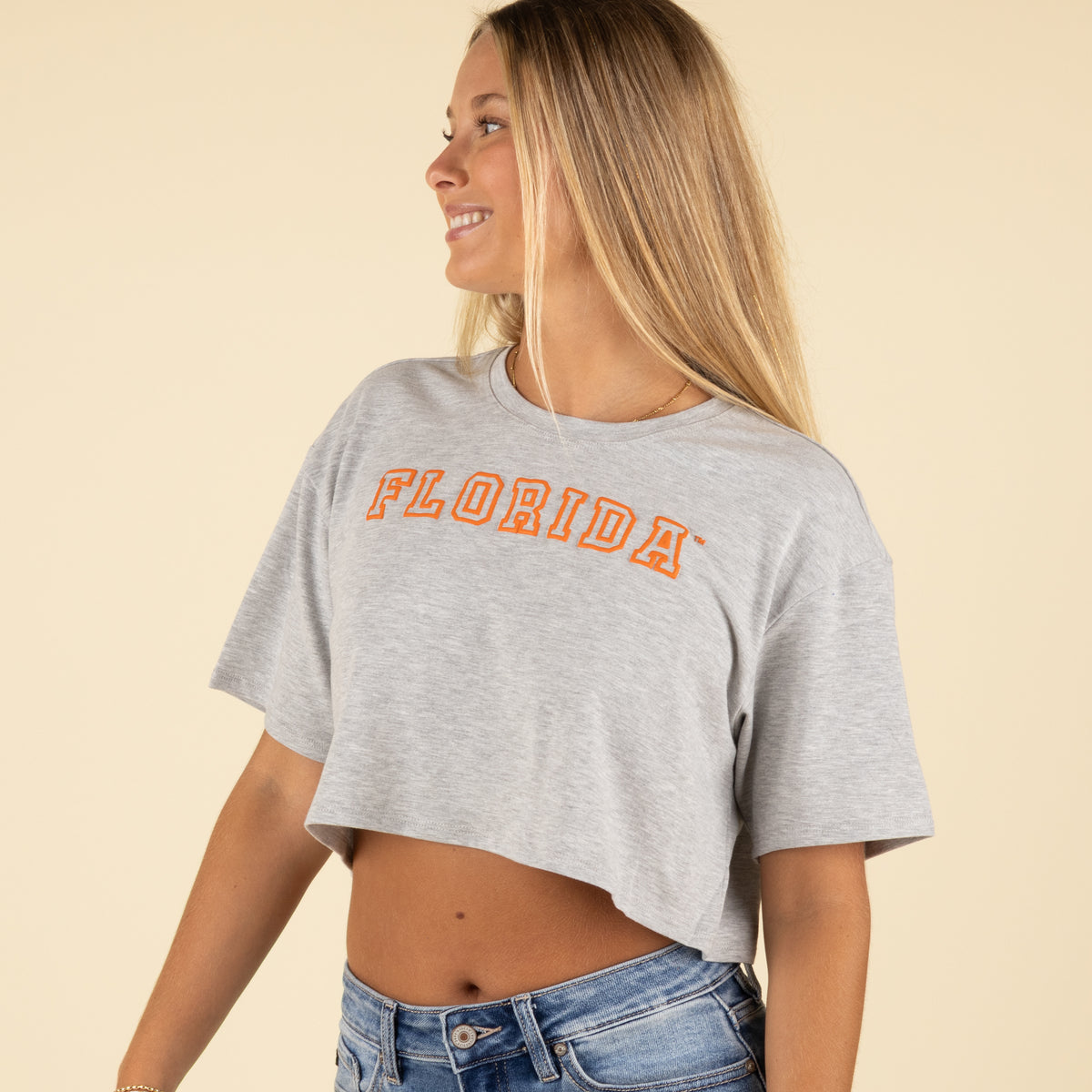 Side view of a woman smiling and wearing a grey Florida cropped t-shirt with orange block lettering and high-rise denim jeans.