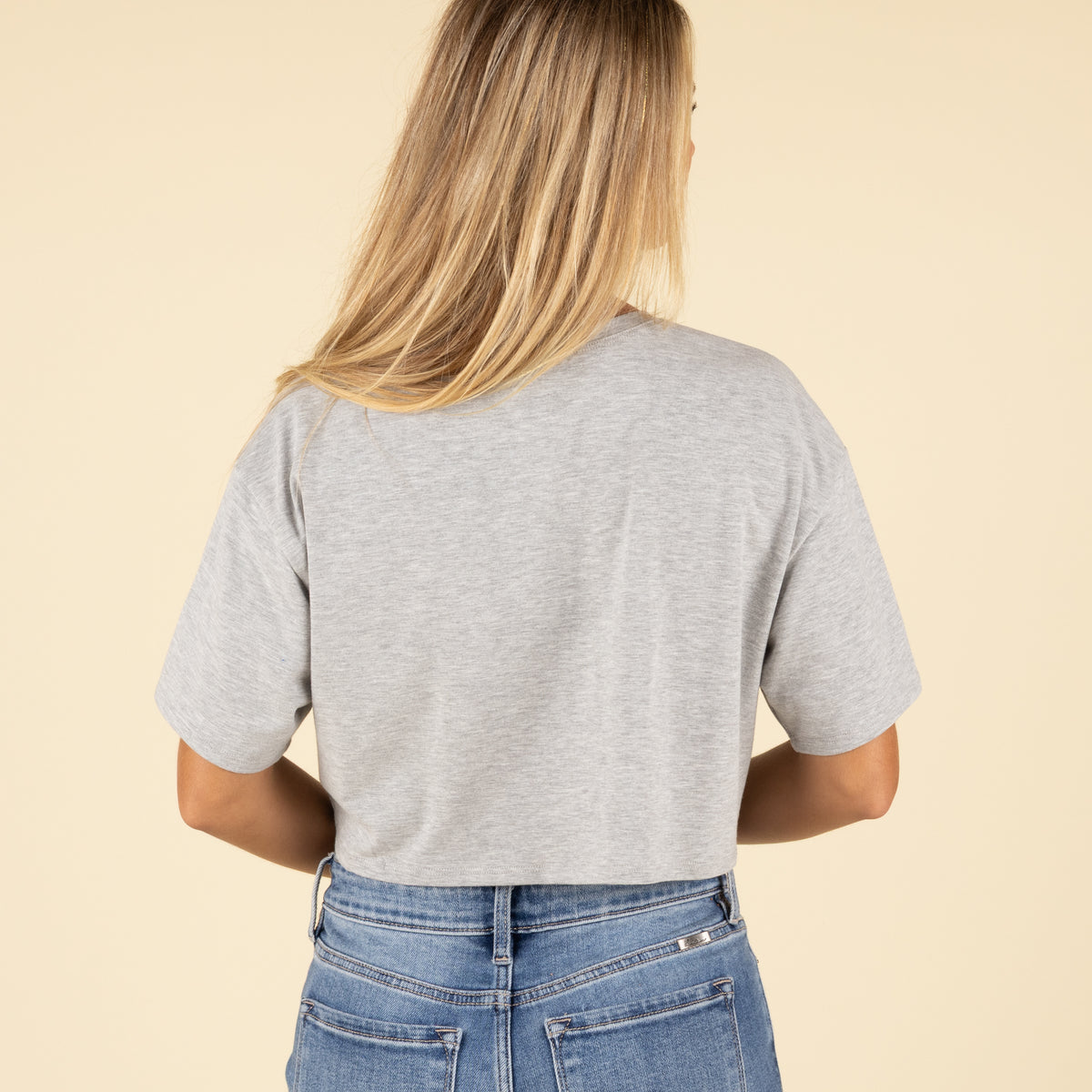 Back view of a woman wearing a plain grey cropped t-shirt with short sleeves and mid-rise blue jeans.
