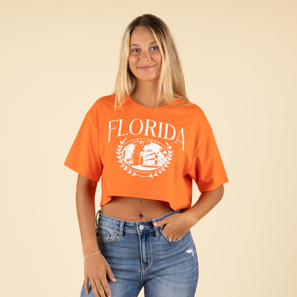 Front view of a woman wearing an orange Florida cropped t-shirt with white collegiate graphic and high-rise ripped jeans.