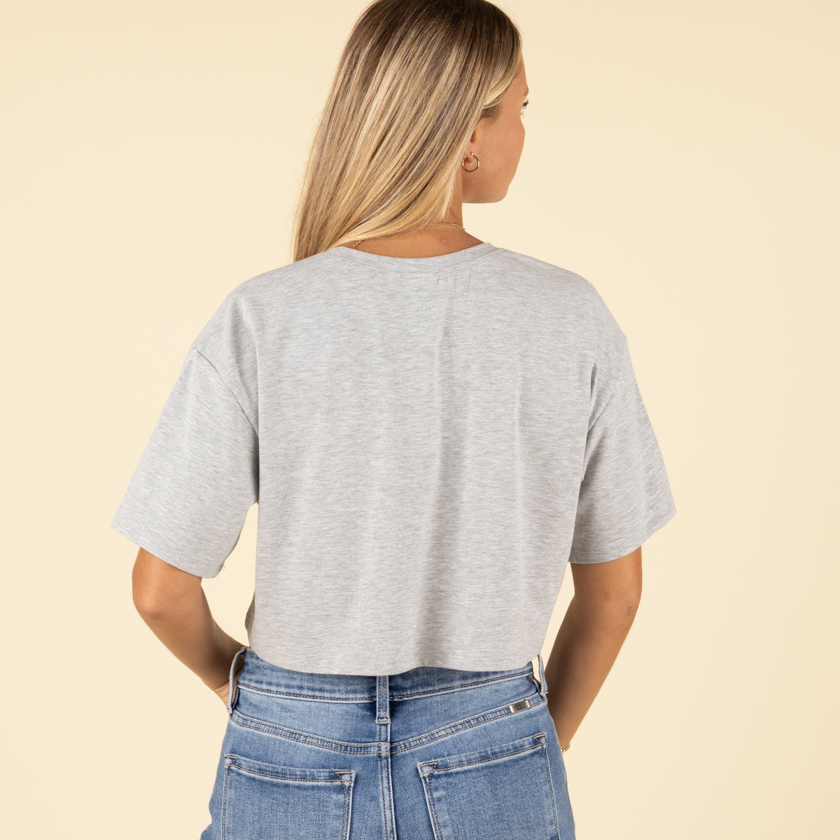 Back view of a woman in a plain grey cropped t-shirt and light-wash high-rise jeans, arms resting by her sides.