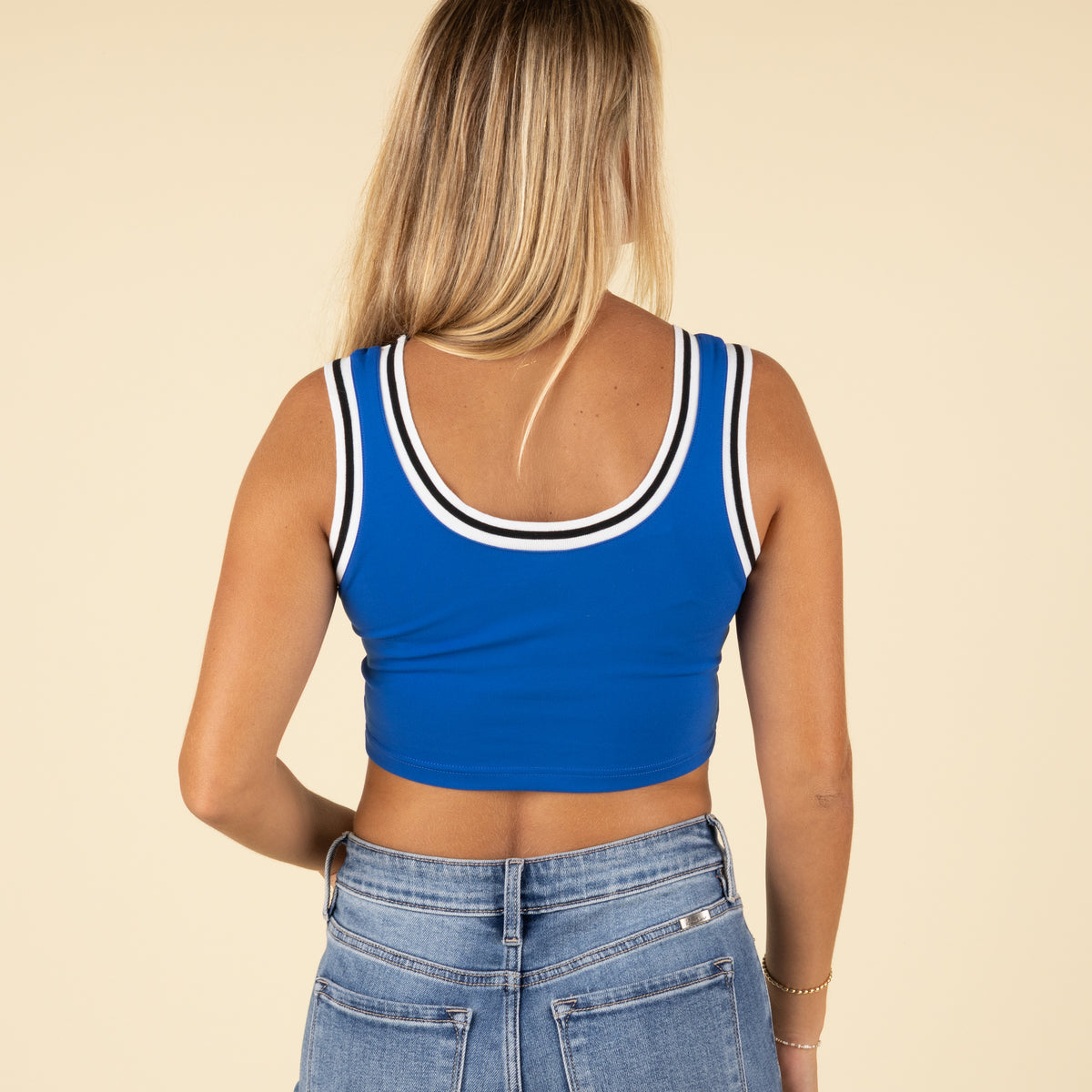 Back view of a woman wearing a royal blue cropped tank top with white and black striped trim and high-rise denim jeans.