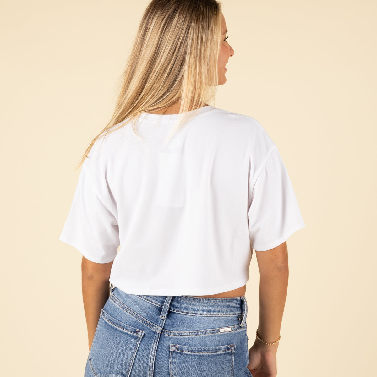 Back view of a woman wearing a plain white cropped t-shirt with short sleeves and light-wash high-rise jeans.
