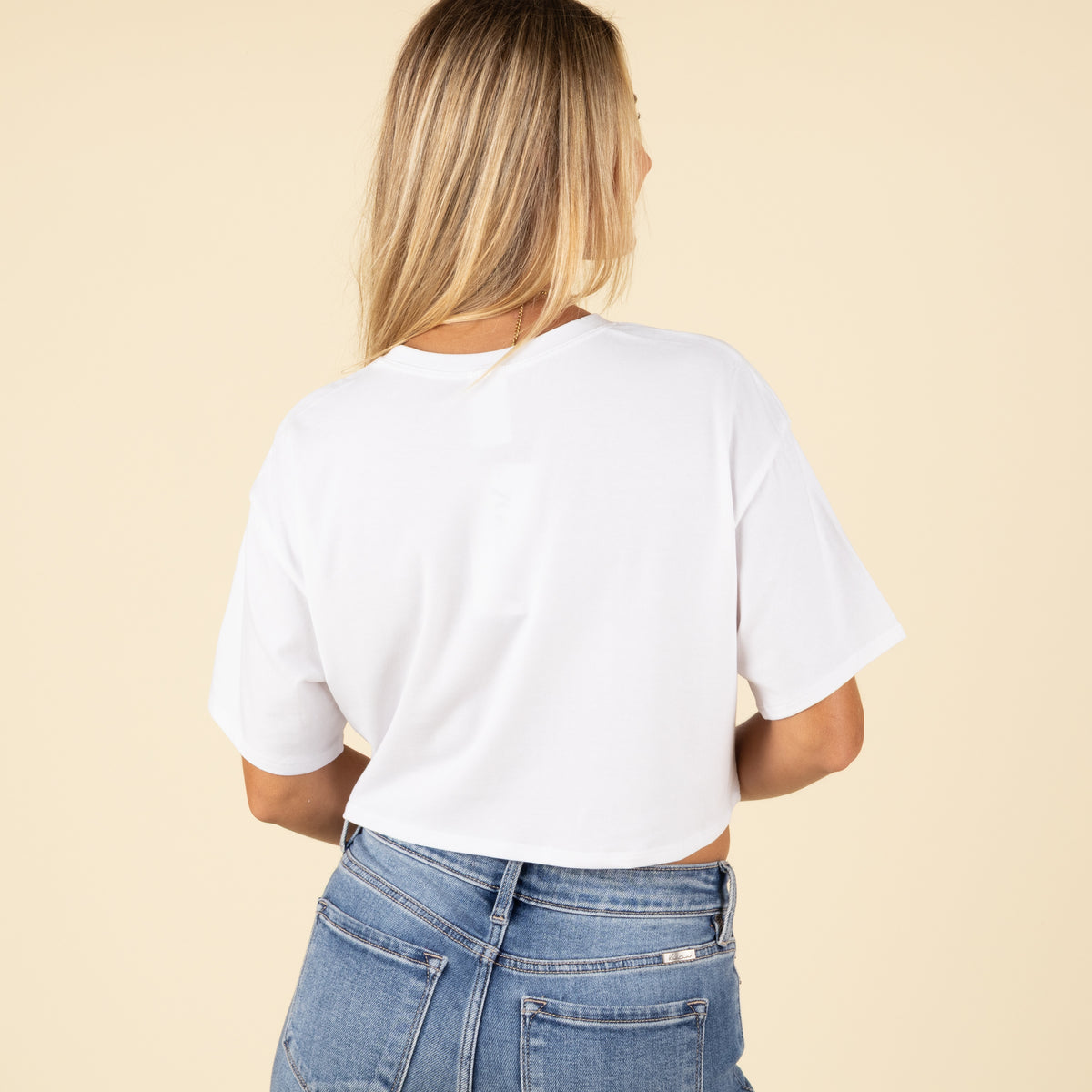 Back view of a woman wearing a plain white cropped t-shirt with short sleeves and high-rise light-wash jeans.