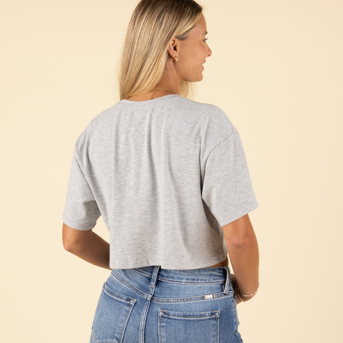 Back view of a woman in a plain grey cropped t-shirt and light-wash high-rise jeans, arms resting by her sides.