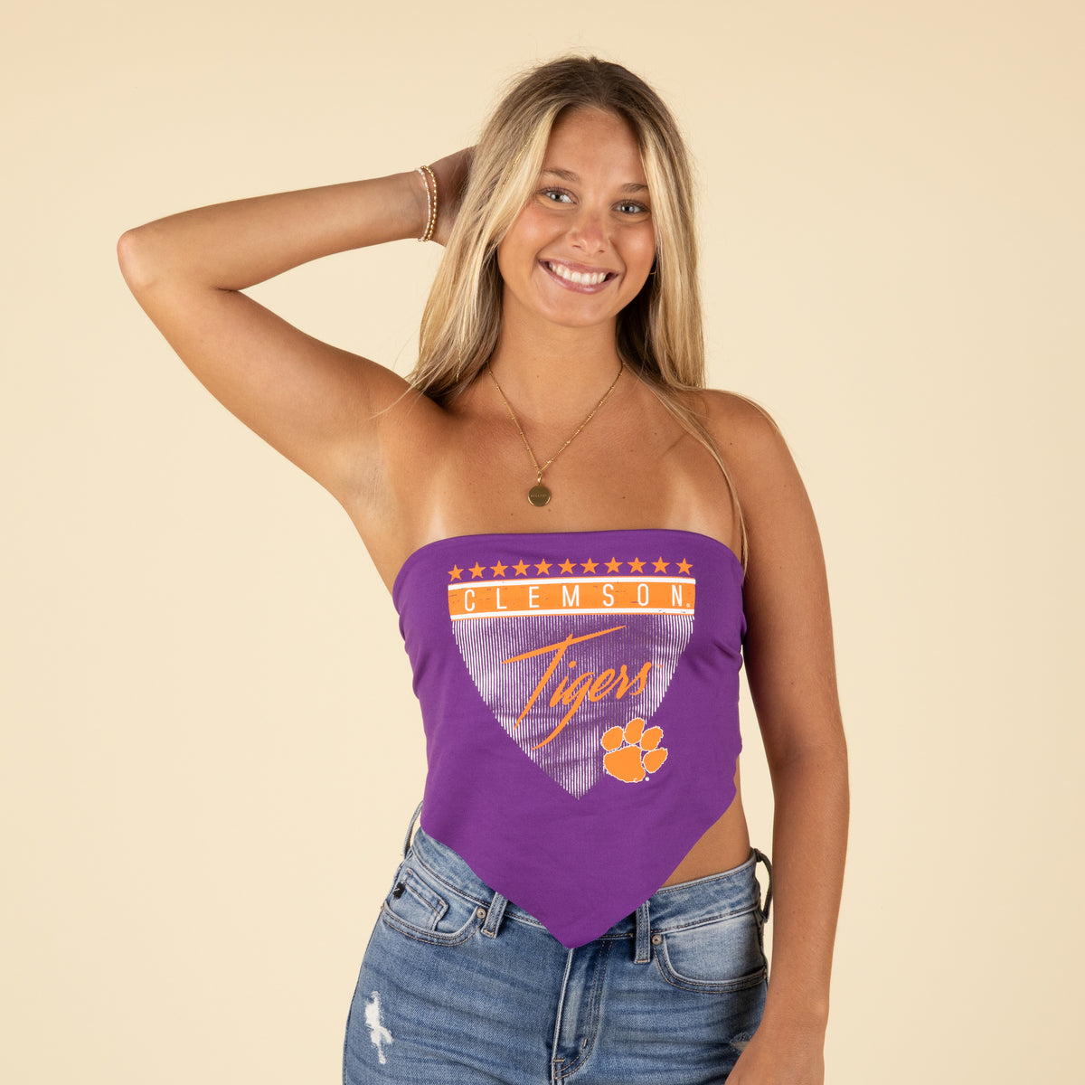 Front view of model in a purple Clemson Tigers bandana tube top with stars and logo design, smiling with hands in hair.