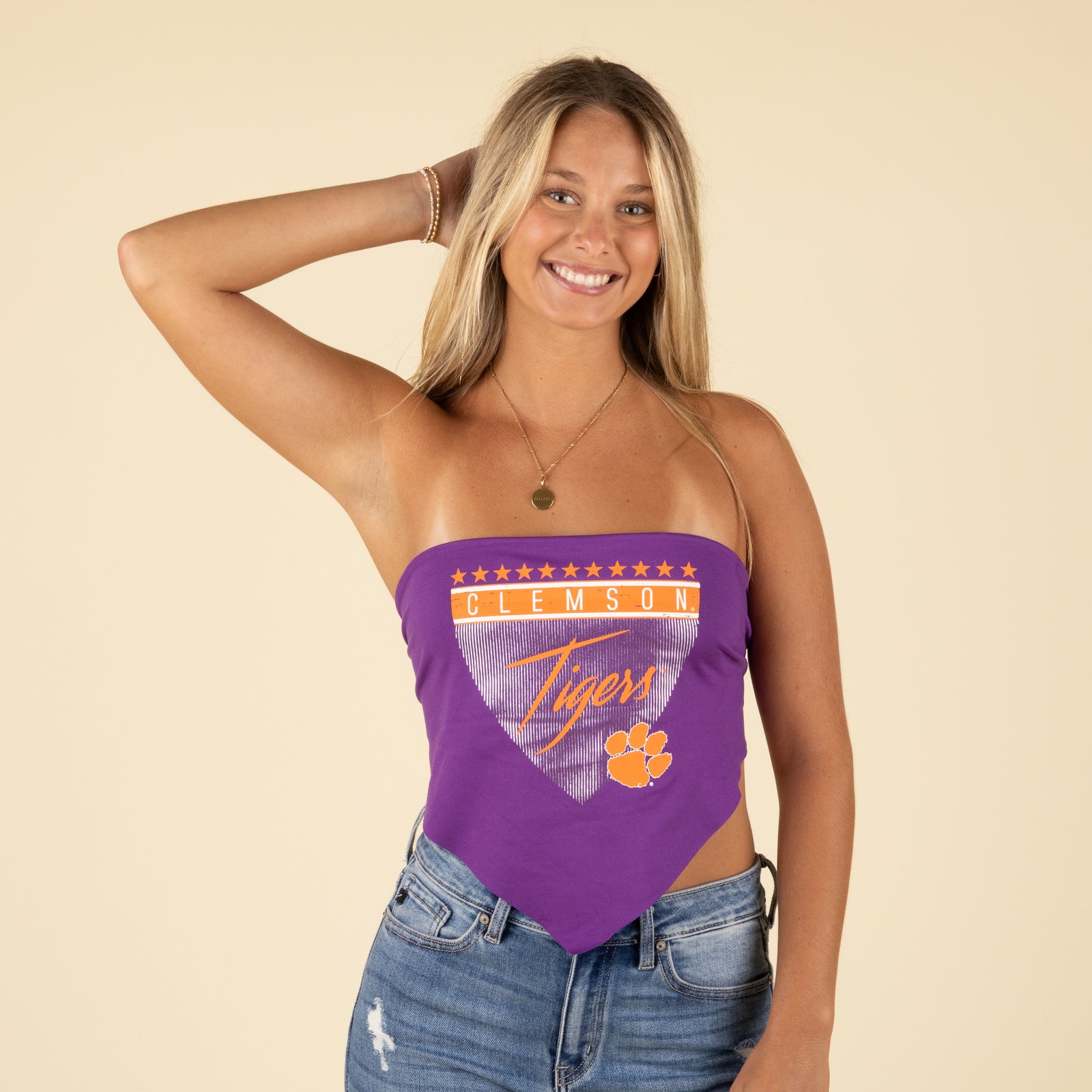 Front view of model in a purple Clemson Tigers bandana tube top with stars and logo design, smiling with hands in hair.