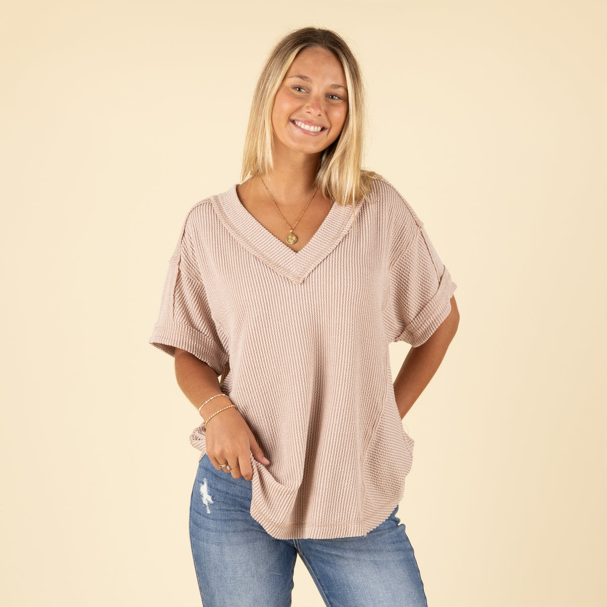 woman wearing a beige ribbed top and blue jeans.