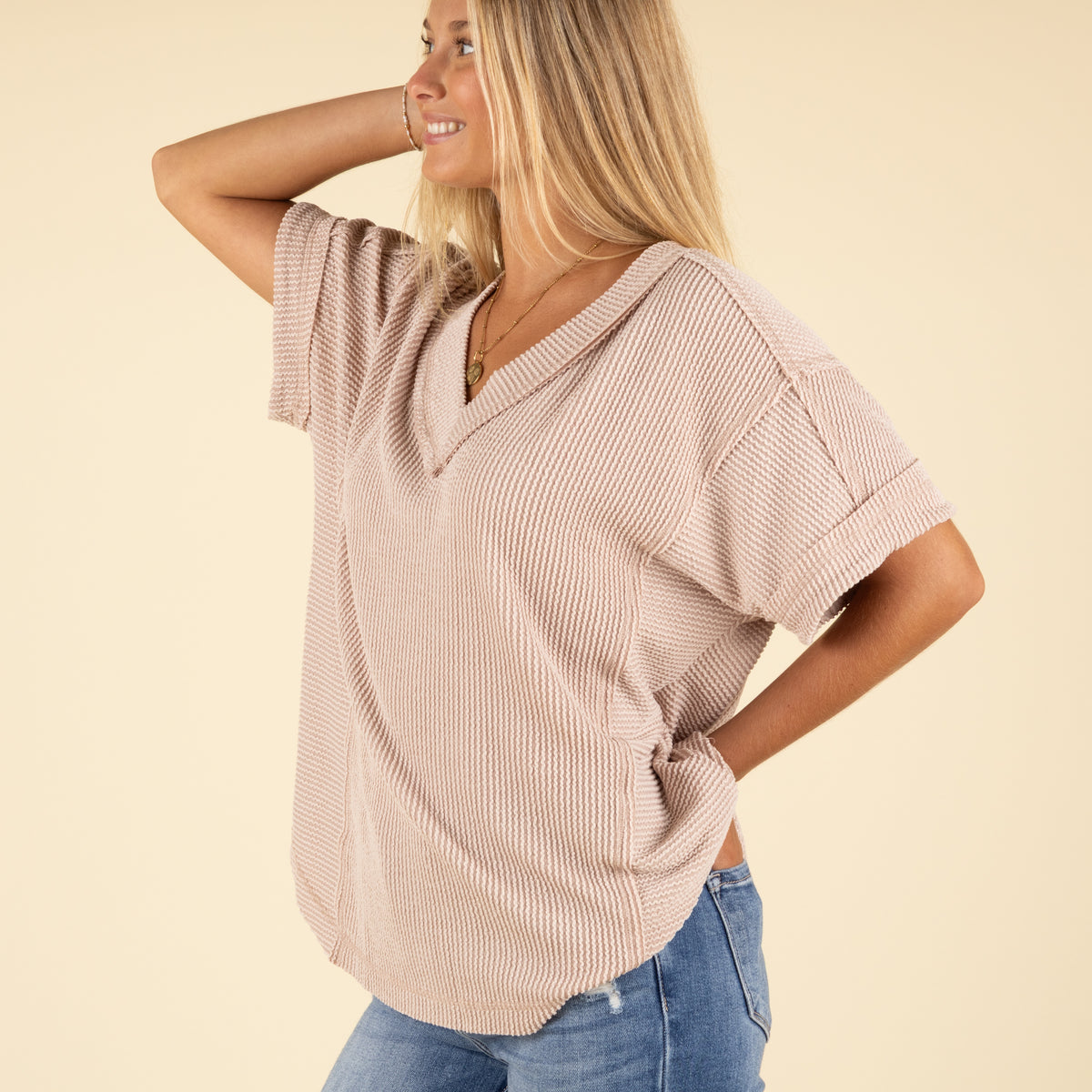 side view of woman wearing a beige ribbed top and blue jeans.