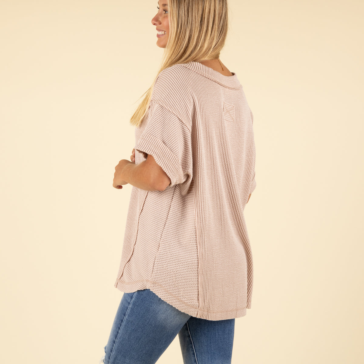 back view of woman wearing a beige ribbed top and blue jeans.