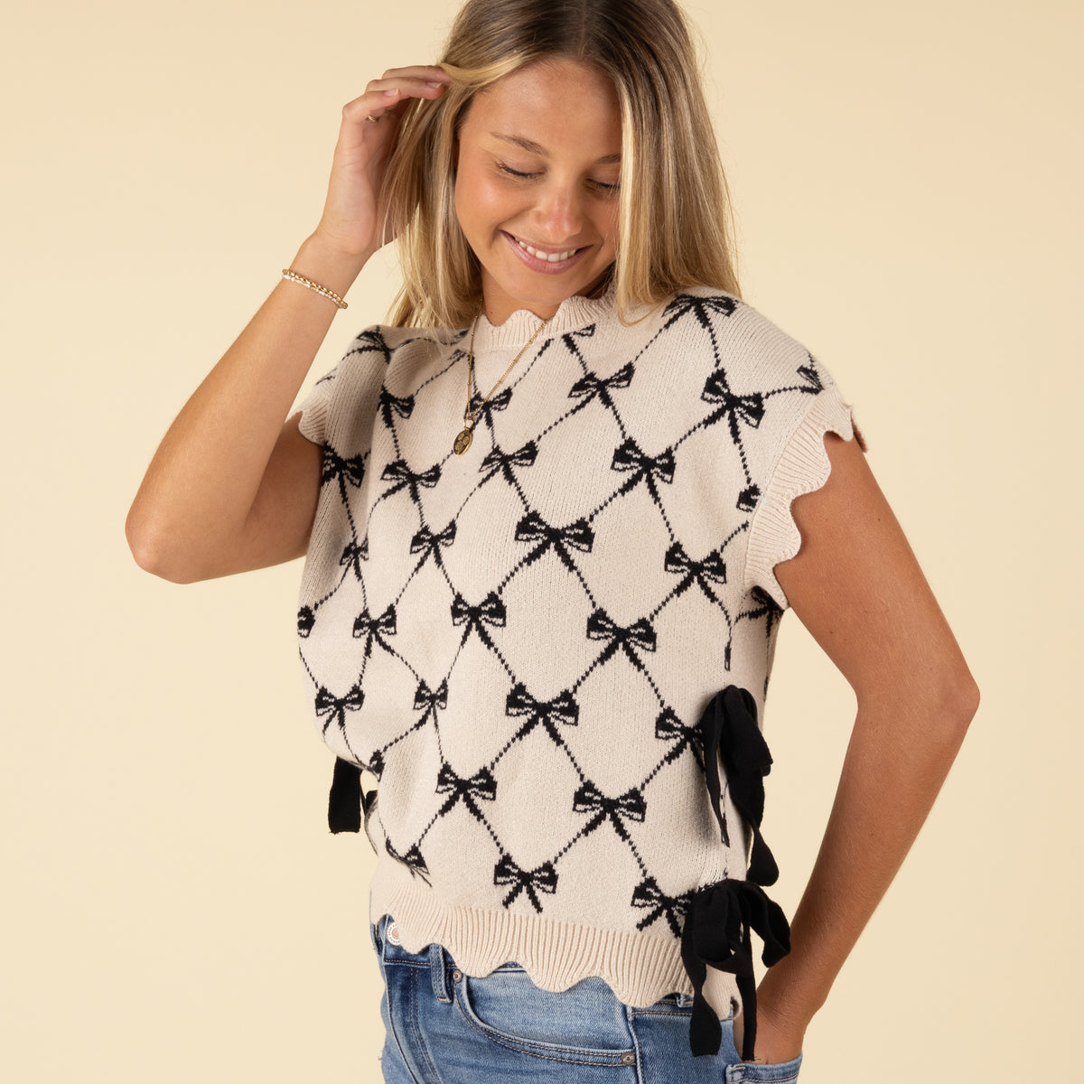 Side angle of ivory bow-pattern sweater with scalloped trim and side ribbon tie details.