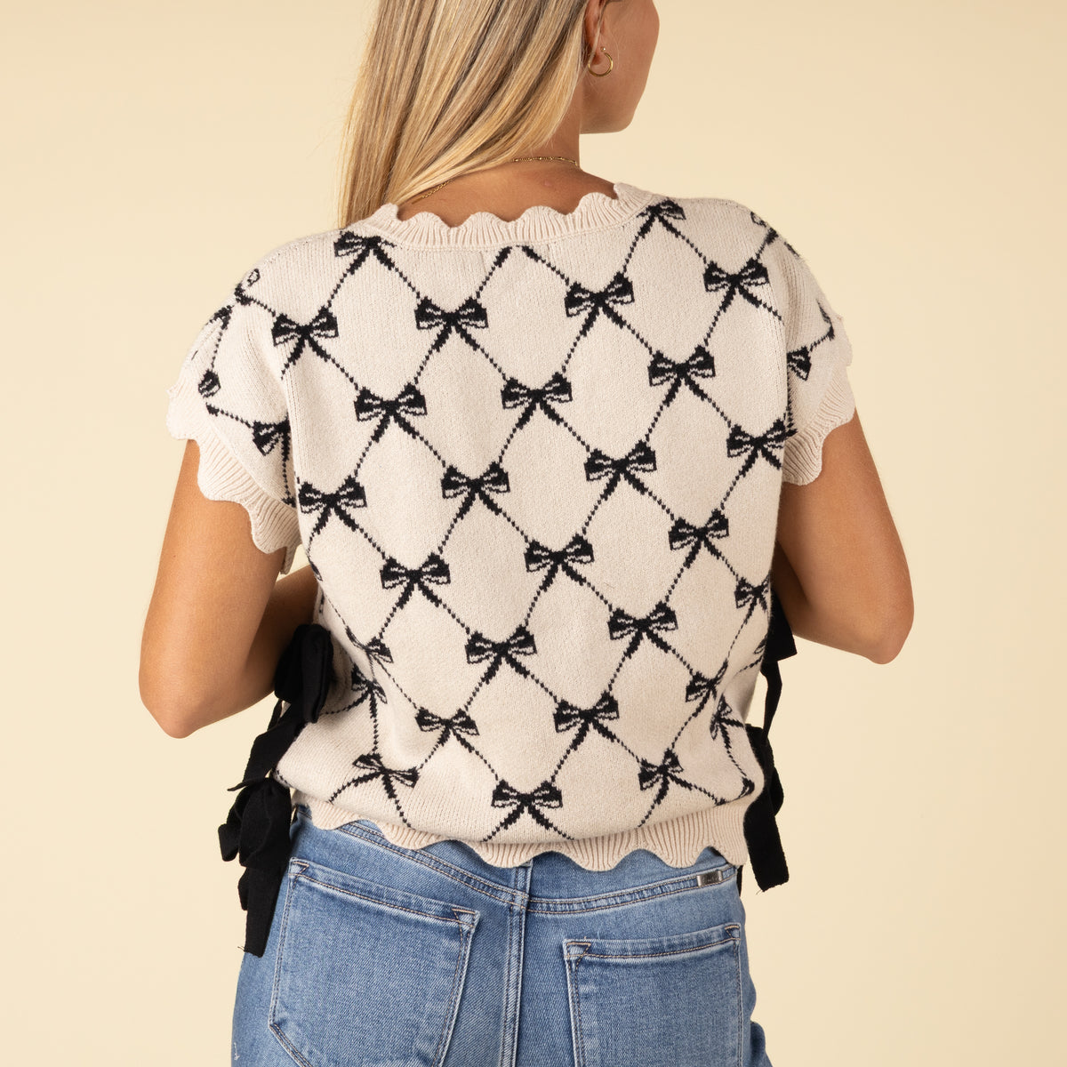 Back view of ivory knit sweater with black bow pattern and scalloped trim, styled with blue jeans.