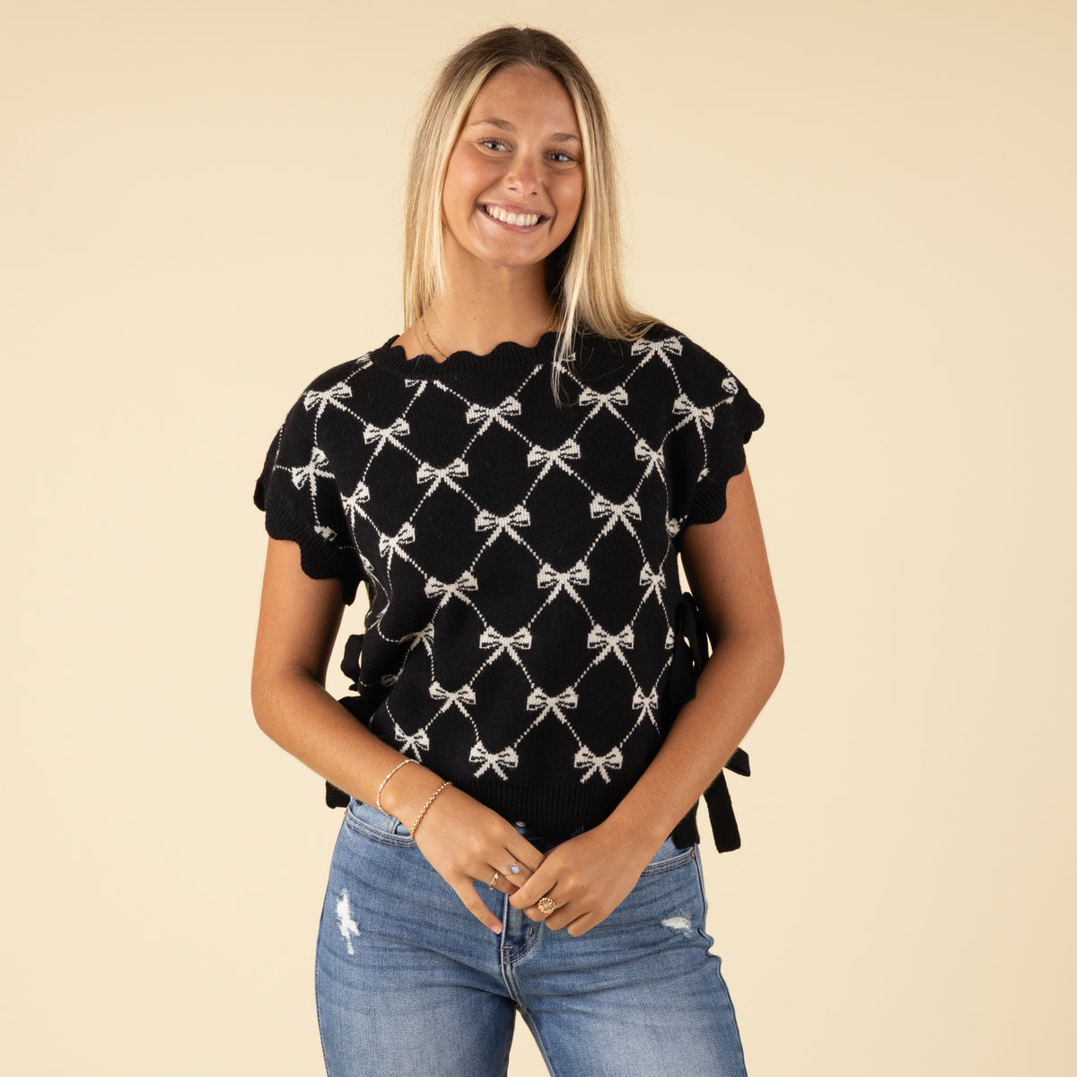 Woman wearing black knit sweater with white bow pattern and scalloped sleeves, smiling at the camera.