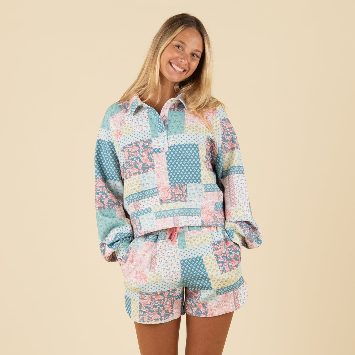 Front view of a smiling woman in a pastel patchwork-print pullover with long sleeves and a relaxed fit.