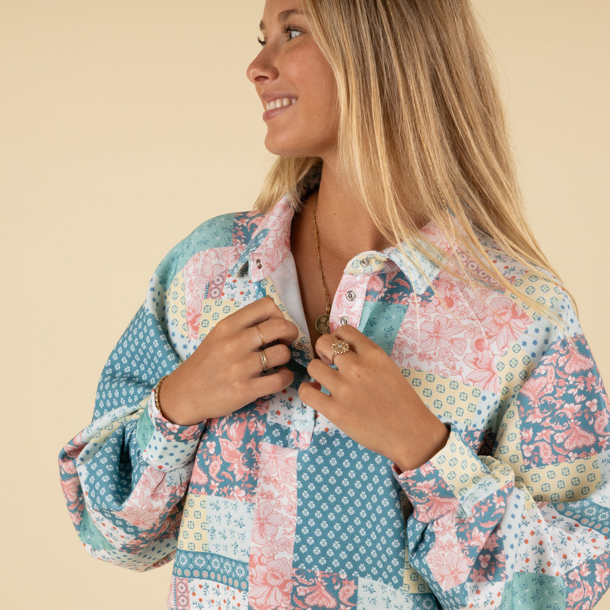 Close-up side view of a woman wearing a pastel patchwork-print pullover, showing the collared neckline and snap button details.