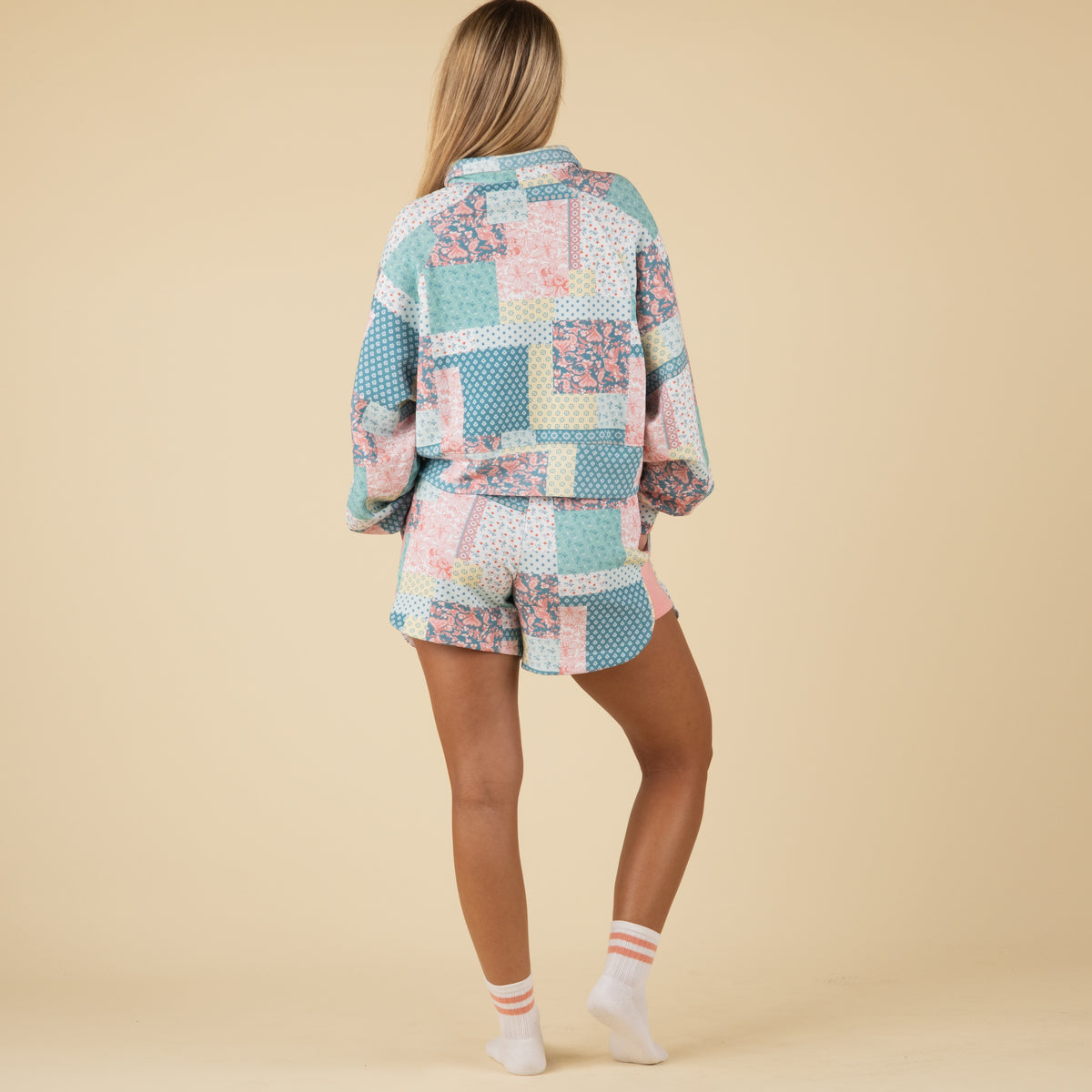 Full back view of a woman wearing pastel patchwork-print shorts with pink side panels, paired with a matching pullover.