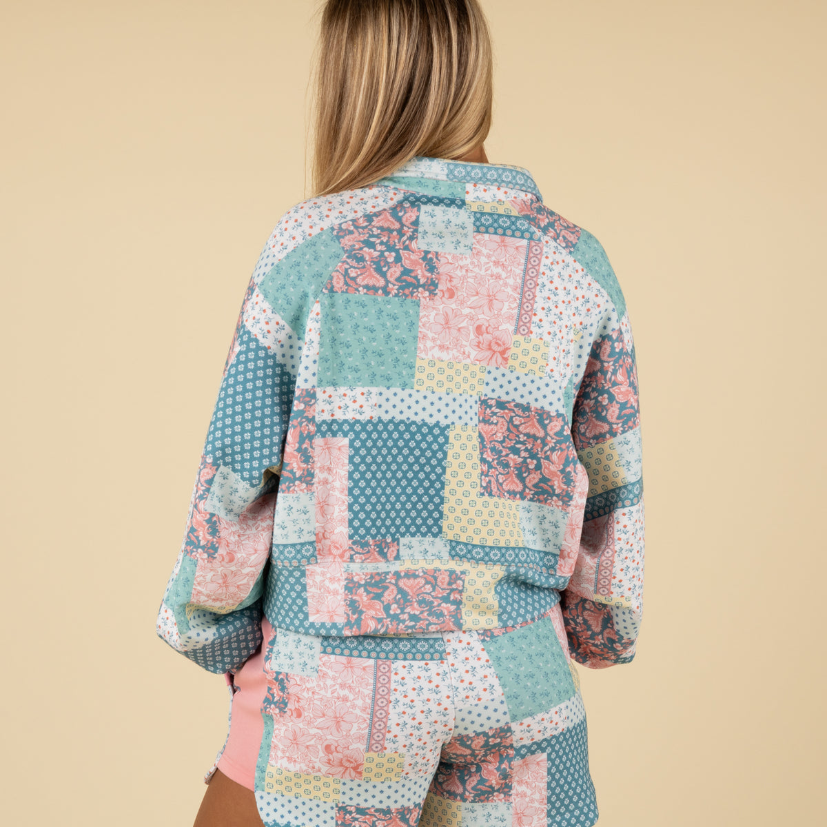 Back view of a woman wearing a pastel patchwork-print long-sleeve pullover with mixed floral and geometric patterns.