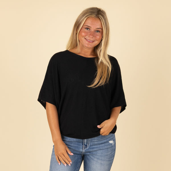  Woman wearing a black loose fit short sleeve top with relaxed sleeves, paired with jeans, front view.