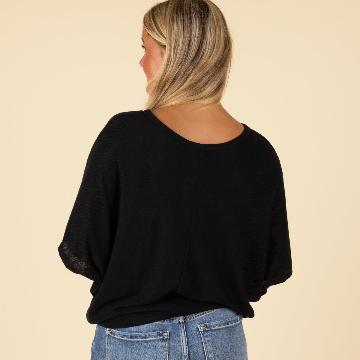 Woman wearing a black loose fit short sleeve top with relaxed sleeves, paired with jeans, back view.