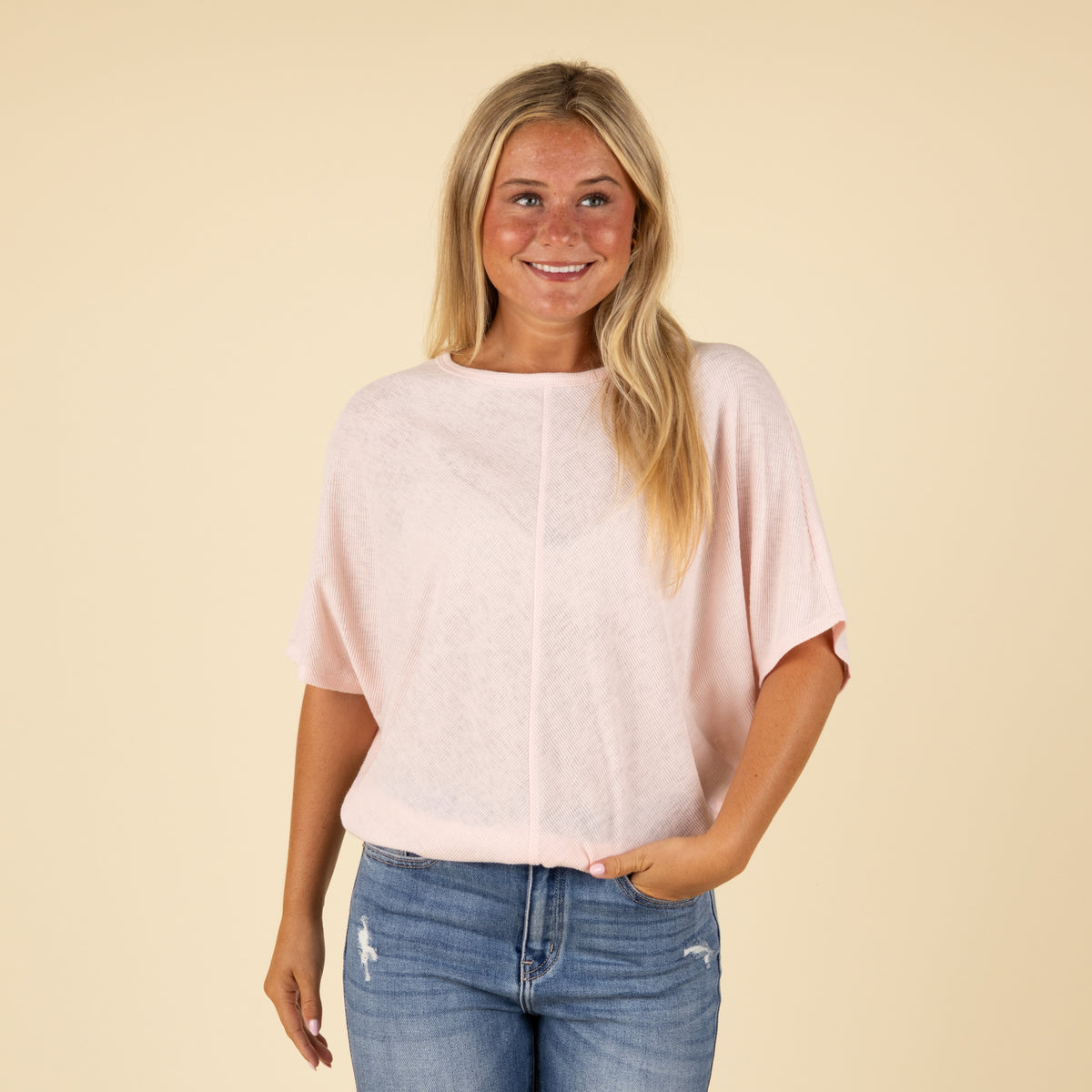 Woman wearing a light pink loose fit short sleeve top with relaxed sleeves, paired with jeans, front view.
