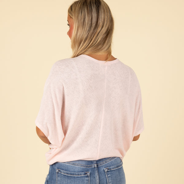  Back view of woman wearing a light pink loose fit short sleeve top with relaxed drape.