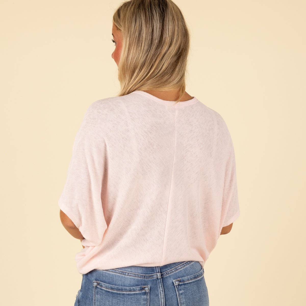 Back view of woman wearing a light pink loose fit short sleeve top with relaxed drape.
