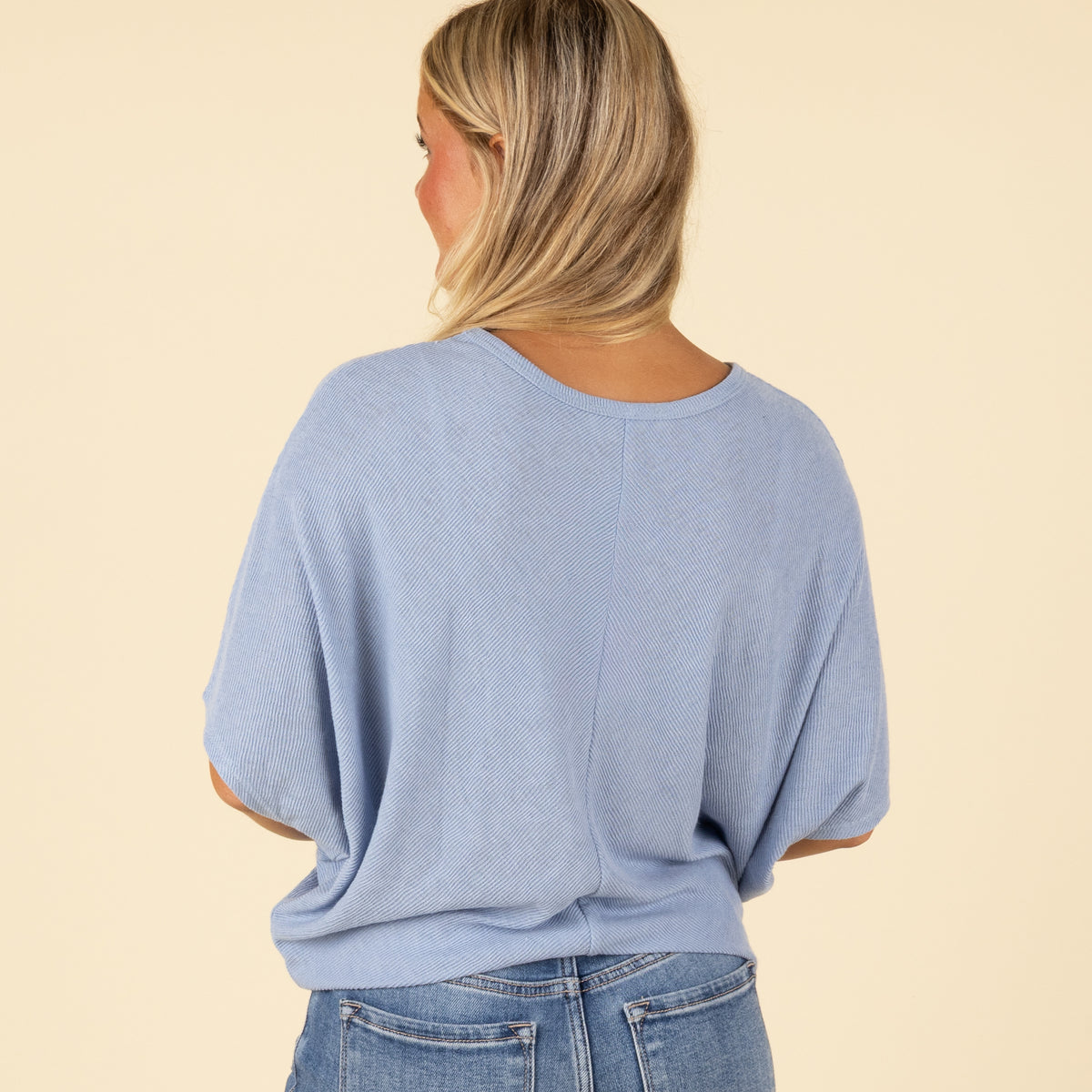 Back view of woman wearing a light blue loose fit short sleeve top with relaxed drape.