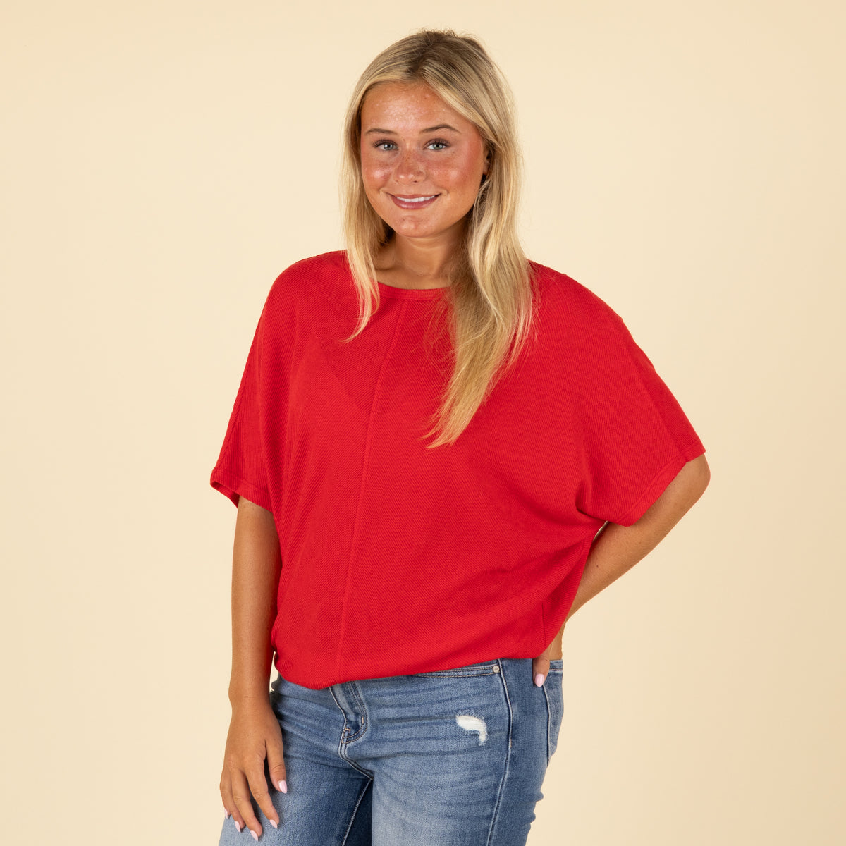 Woman wearing a red loose fit short sleeve top with relaxed sleeves, paired with jeans, side view.