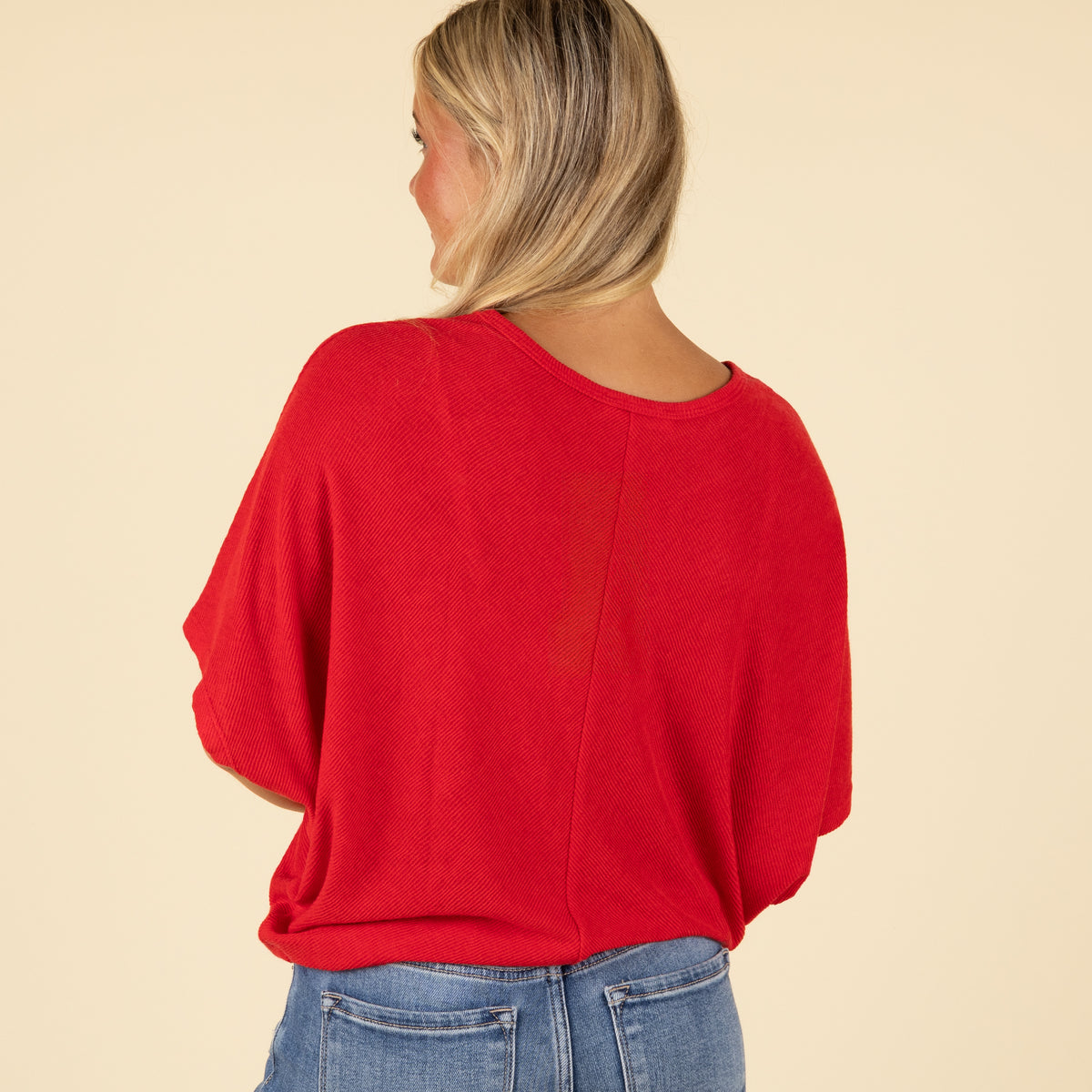 Woman wearing a red loose fit short sleeve top with relaxed sleeves, paired with jeans, back view.