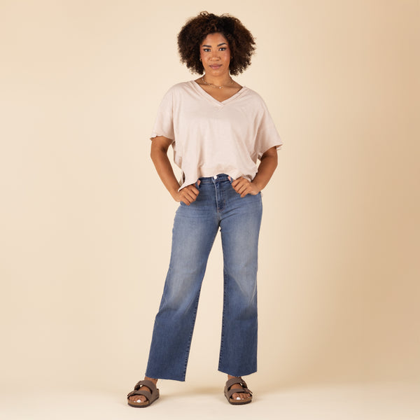 Front view of Just Black Denim Palazzo Jeans in medium wash with high-rise waist and wide-leg cut. Styled with a light taupe top and sandals.