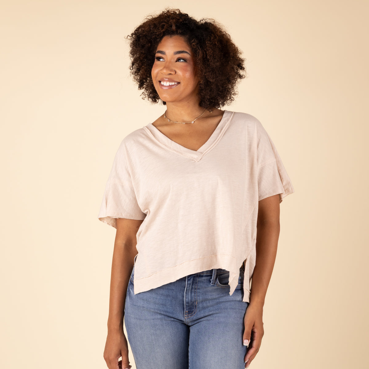 Woman wearing a beige top and blue jeans against a beige background