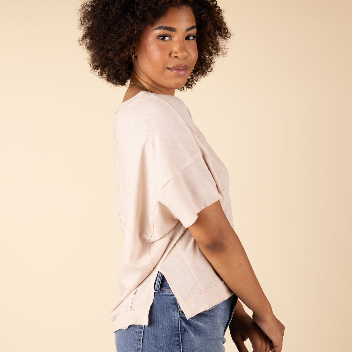 Woman wearing a beige top and blue jeans against a beige background
