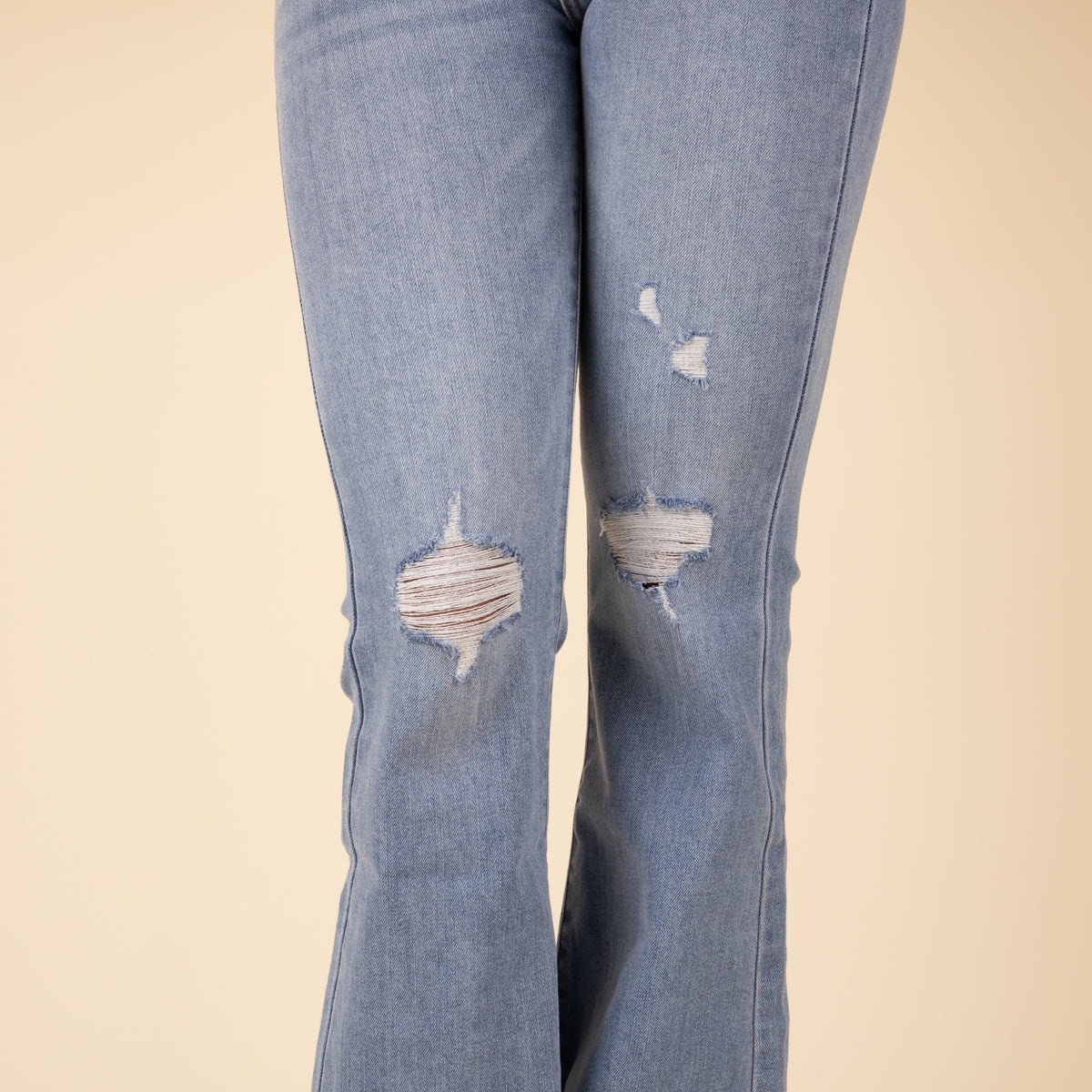 Close-up view of the front thigh distressing on light-wash flare jeans, showing large frayed holes and subtle abrasions on stretchy denim fabric.