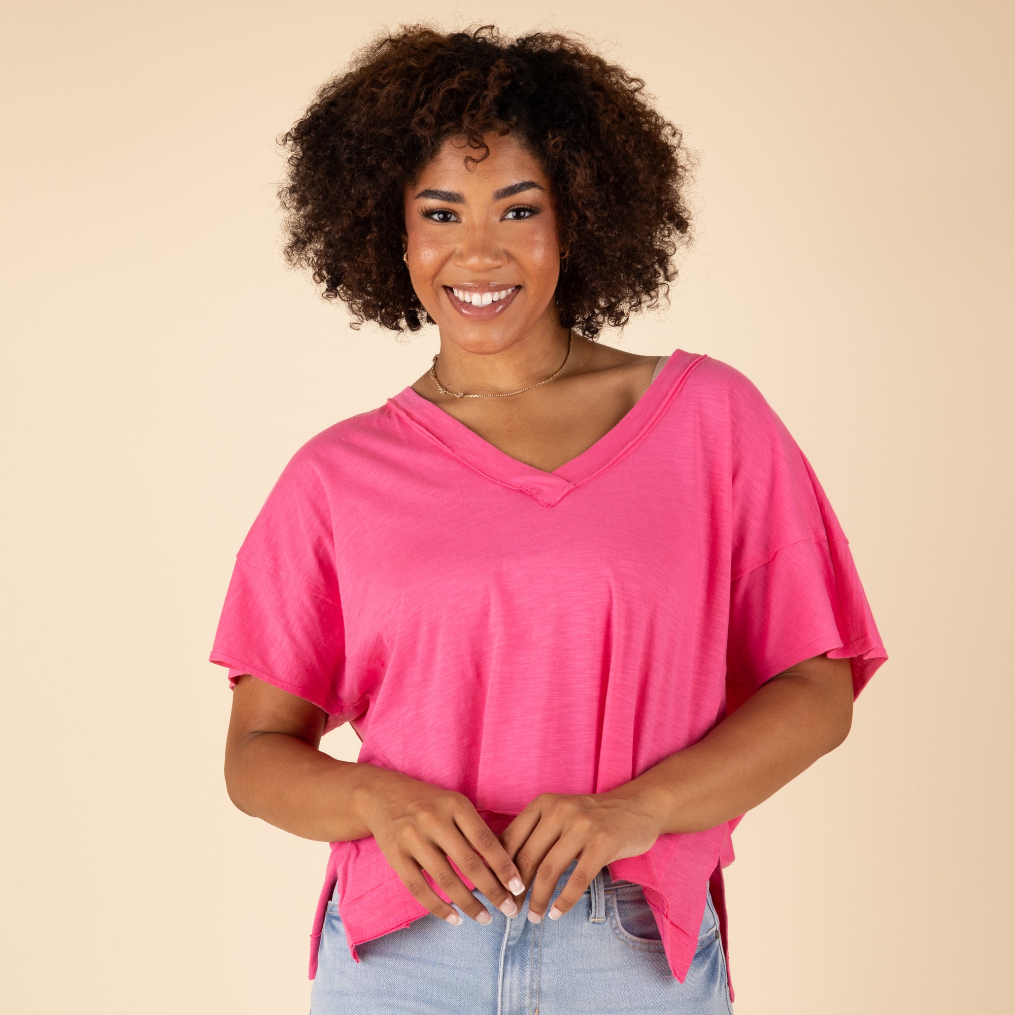 Woman wearing a pink top and light blue jeans against a beige background