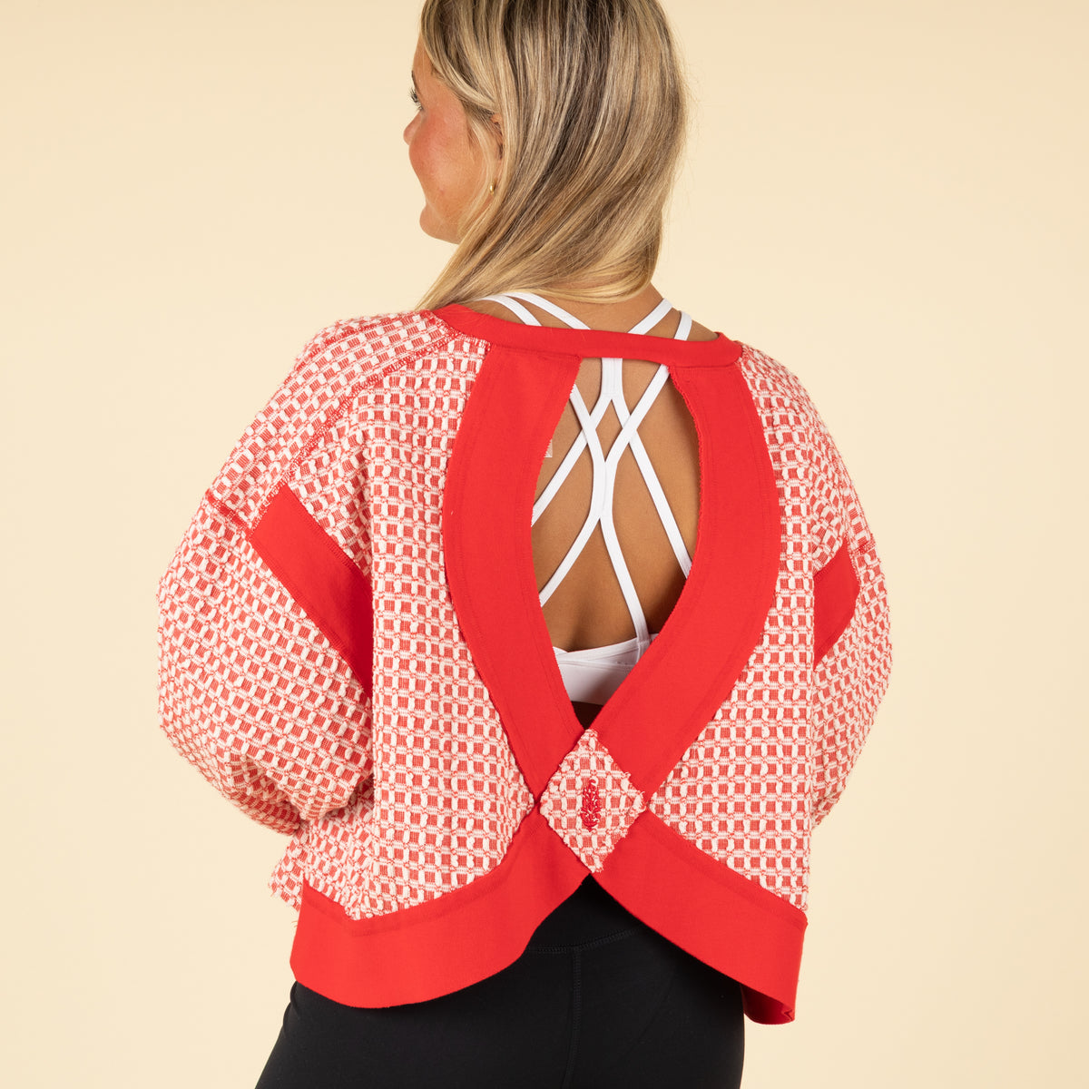 Woman wearing a red and white patterned top with an open back on a beige background
