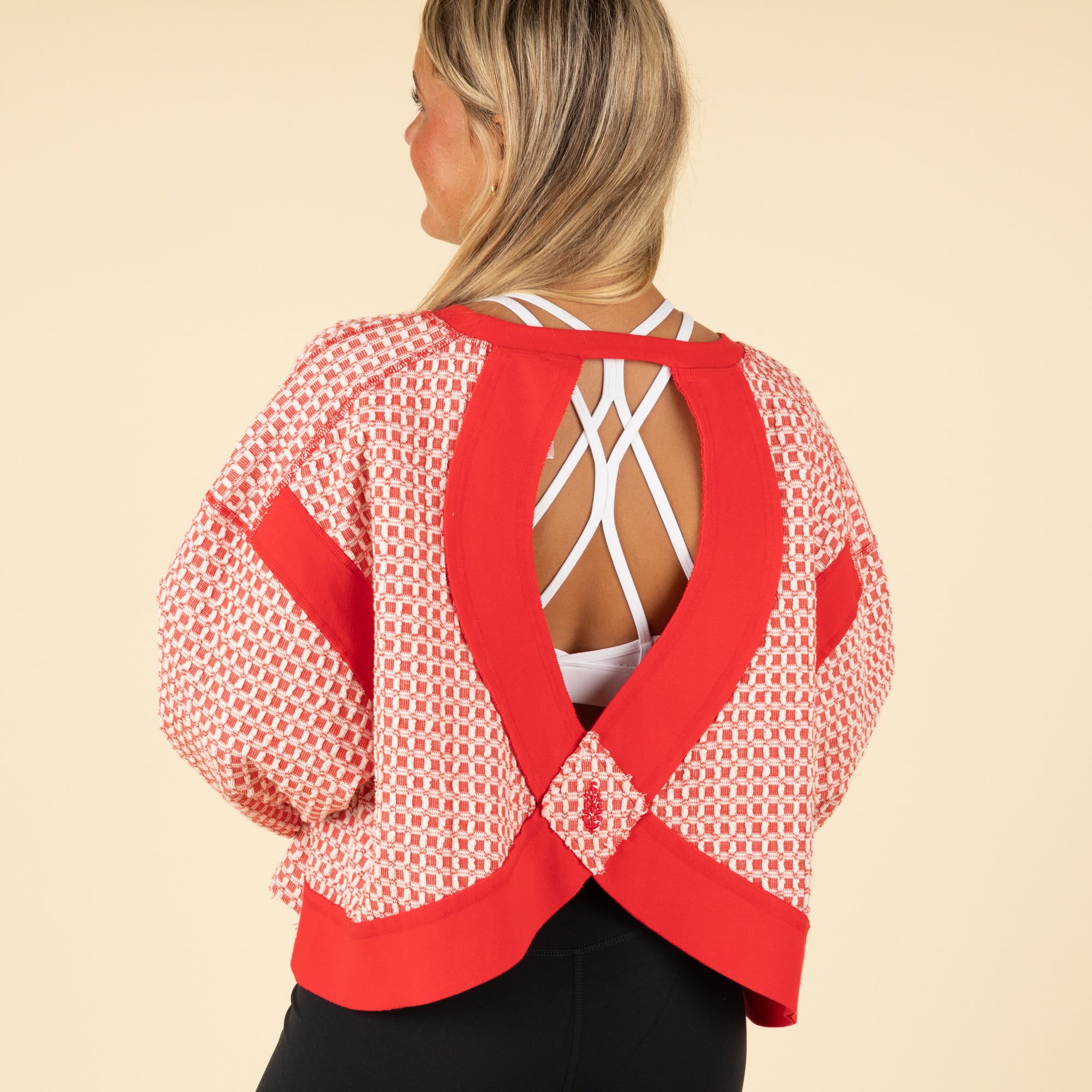 Woman wearing a red and white patterned top with an open back on a beige background